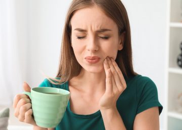 woman with coffee mug touching her cheek in pain